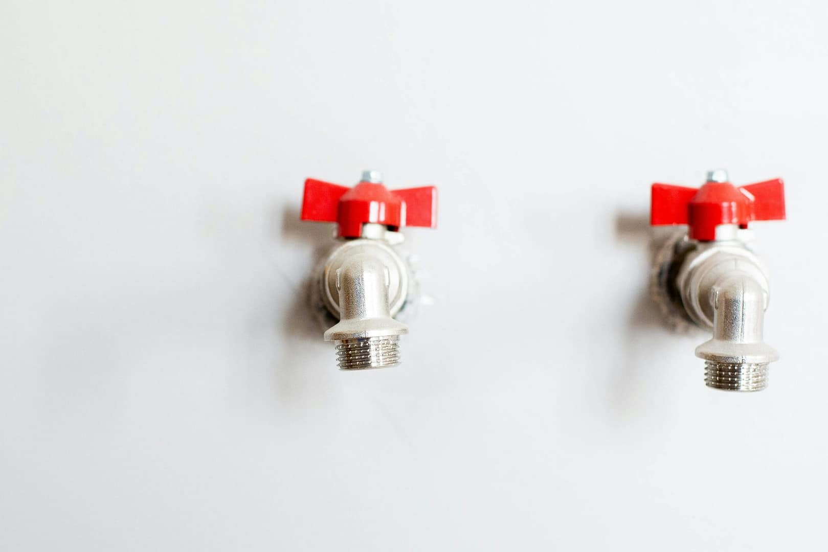 Close-up of two metal faucets with red handles against a white wall, showcasing plumbing detail.