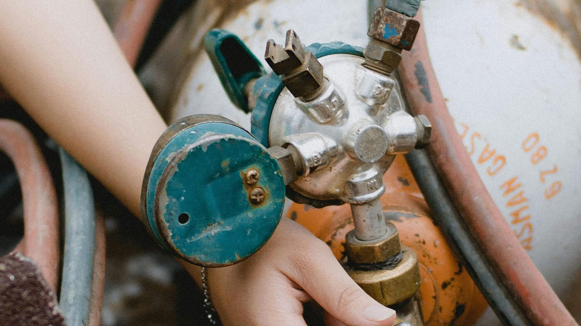 A technician's hands adjusting a gas cylinder valve with hoses.