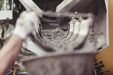 building-construction-building-site-constructing-2469 Close-up of concrete being poured from a mixer truck at a construction site with a worker's hand visible.