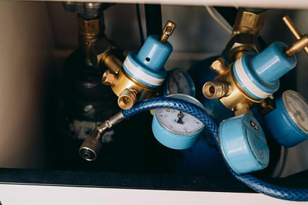 pexels-photo-8943269-8943269 Detailed view of blue and brass gas pressure regulators with gauges and tubing in an industrial setting.