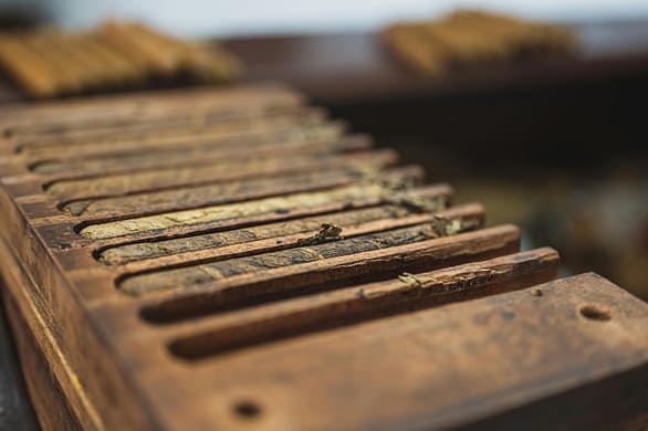 pexels-photo-3975066-3975066 From above closeup of wooden box with narrow rectangular sections with ribbed surface for cigars near table with pile of raw tobacco products in factory